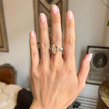 Hand wearing a Vintage, 1980s large yellow sapphire & diamond three-stone ring in yellow gold on a blurred indoor background