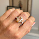 Hand wearing a Vintage, 1980s yellow sapphire & diamond three-stone engagement ring in yellow gold on a neutral background