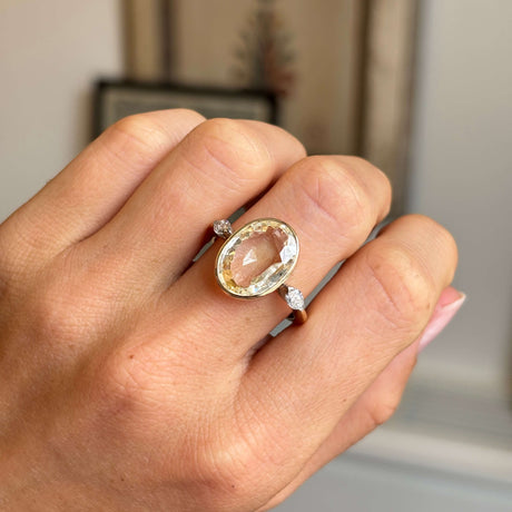 Hand wearing a Vintage, 1980s yellow sapphire & diamond three-stone engagement ring in yellow gold on a neutral background