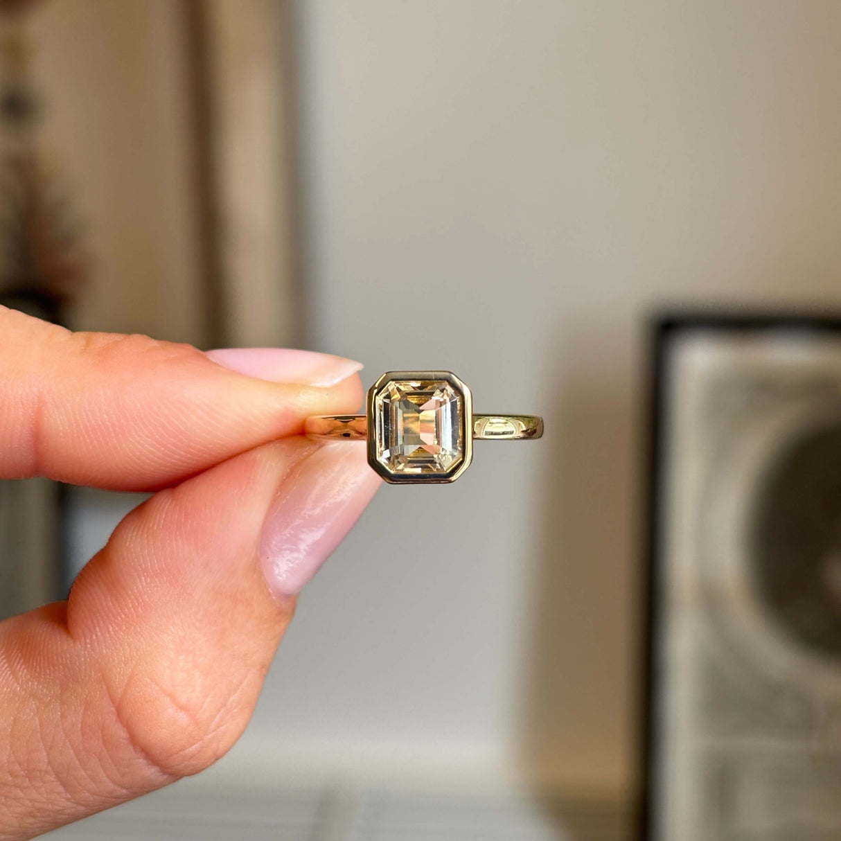 Antique-inspired yellow sapphire solitaire engagement ring in gold held by a hand against a neutral background