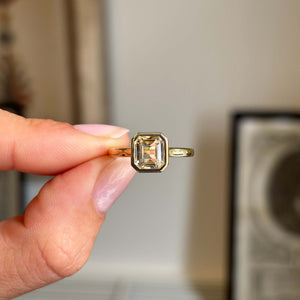 Antique-inspired yellow sapphire solitaire engagement ring in gold held by a hand against a neutral background