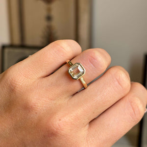 Antique-inspired champagne yellow sapphire solitaire engagement ring in gold on a person's finger against a neutral background