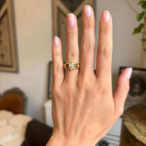Hand wearing a gold Antique, Edwardian yellow diamond solitaire gypsy, set against a blurred indoor background.