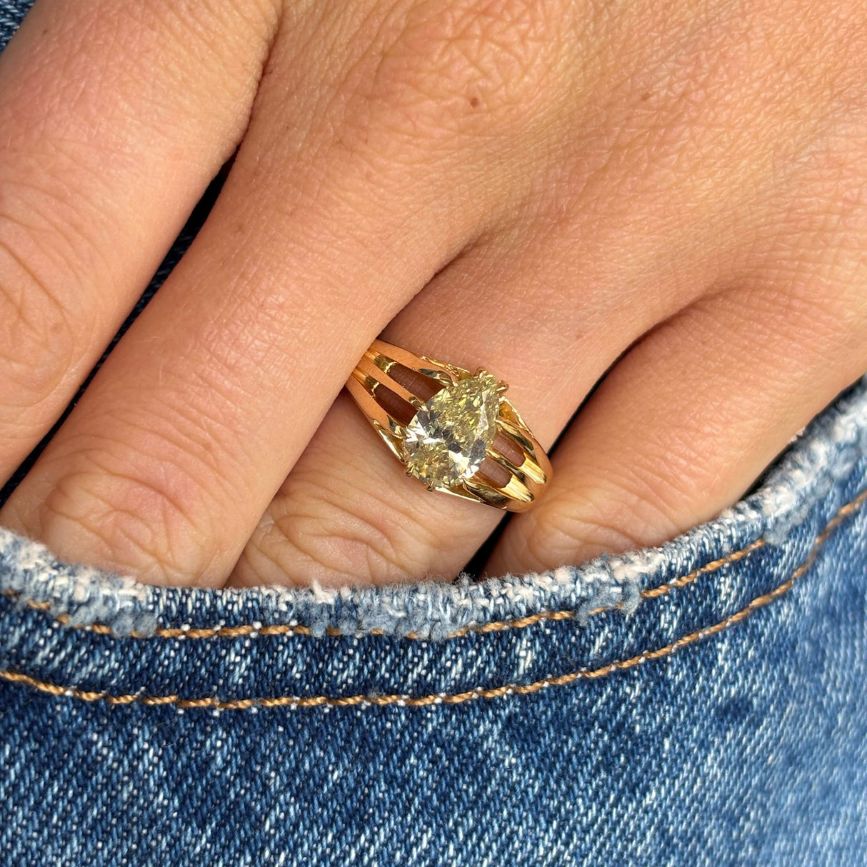 Antique, Edwardian yellow diamond solitaire gypsy ring in yellow gold  on a person's finger wearing blue jeans.