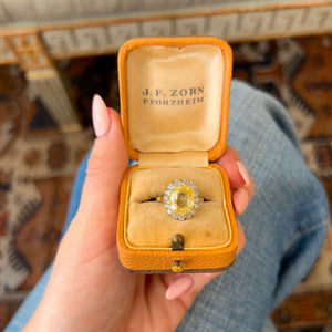 A vintage yellow sapphire cluster engagement ring displayed in an open vintage yellow ring box.