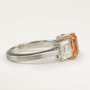 Lab-pink diamond and white diamond three-stone ring placed on a white surface, showing the elegant proportions and gemstones.