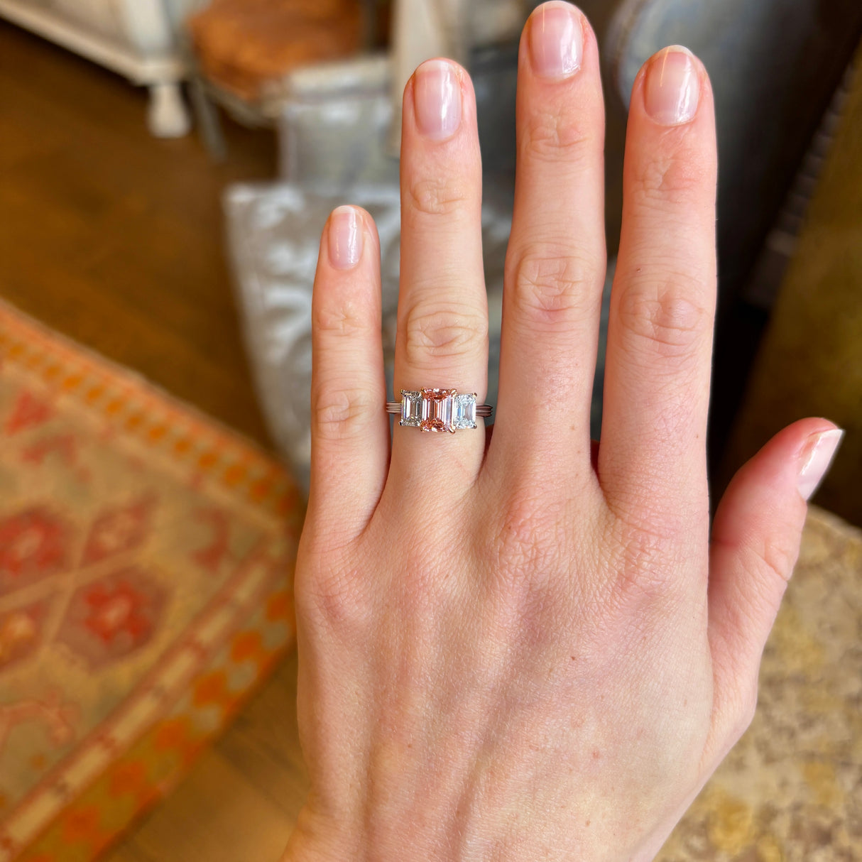 Lab-pink diamond and white diamond three-stone ring worn on the engagement ring finger, demonstrating scale and everyday wear.