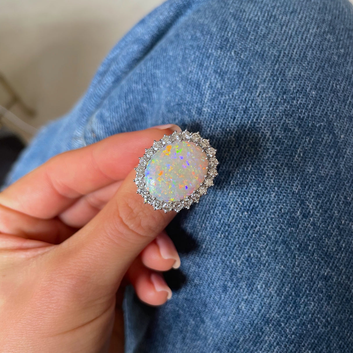 White opal and diamond cluster ring, front view, held in fingers.