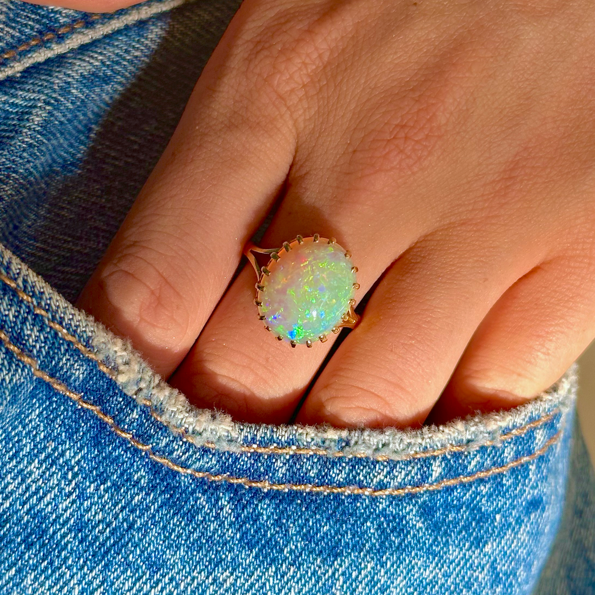 cabochon white opal cocktail ring with 18ct yellow gold band, worn on hand in pocket of jeans, front view. 