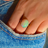 cabochon white opal cocktail ring with 18ct yellow gold band, worn on hand in pocket of jeans, front view. 