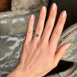 Teal sapphire and diamond three-stone engagement ring with oval-cut centre stone, displayed on a hand, emphasising its sparkling diamonds and rich colour from a distance.