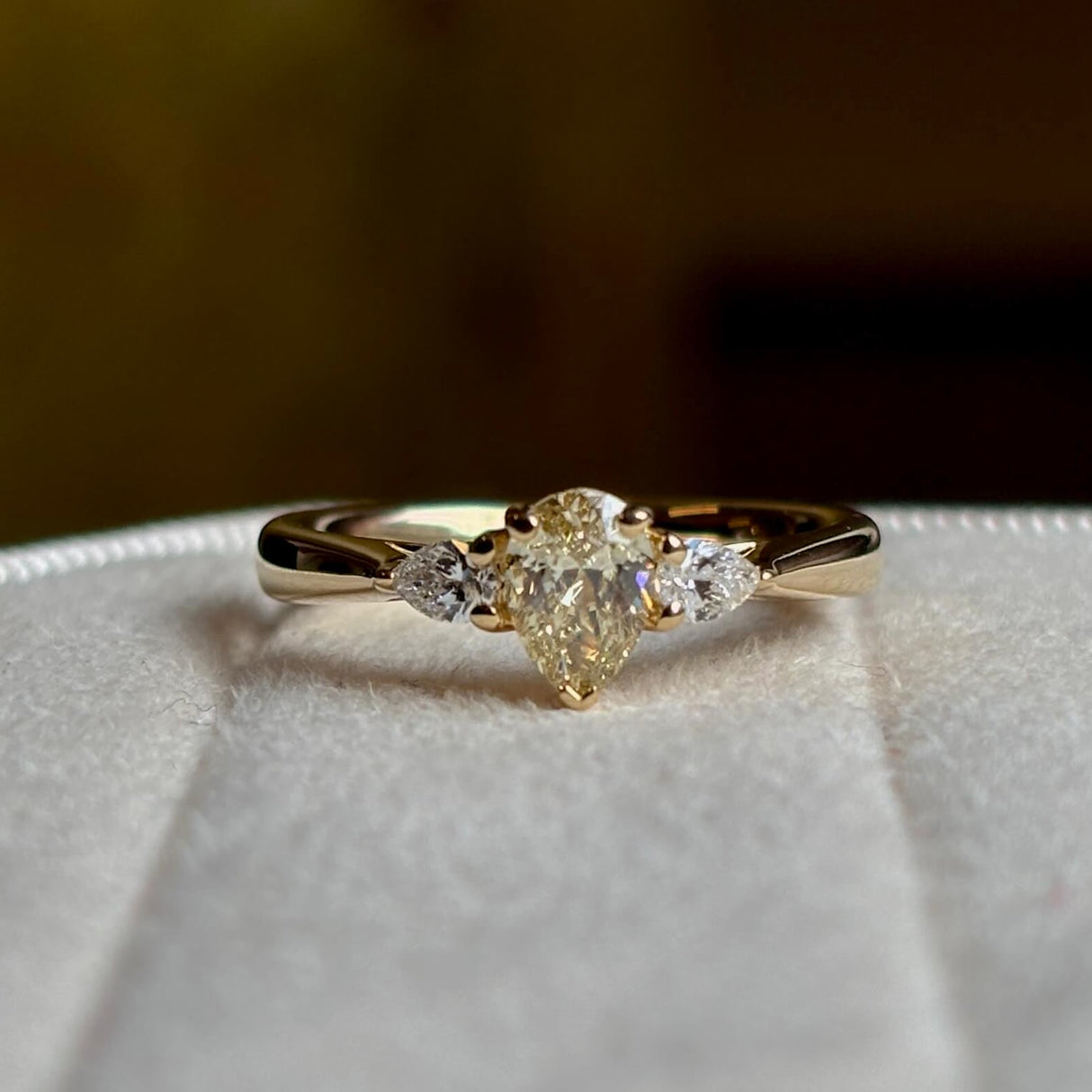 Pear-cut diamond three-stone engagement ring on a blurred background showing details. 