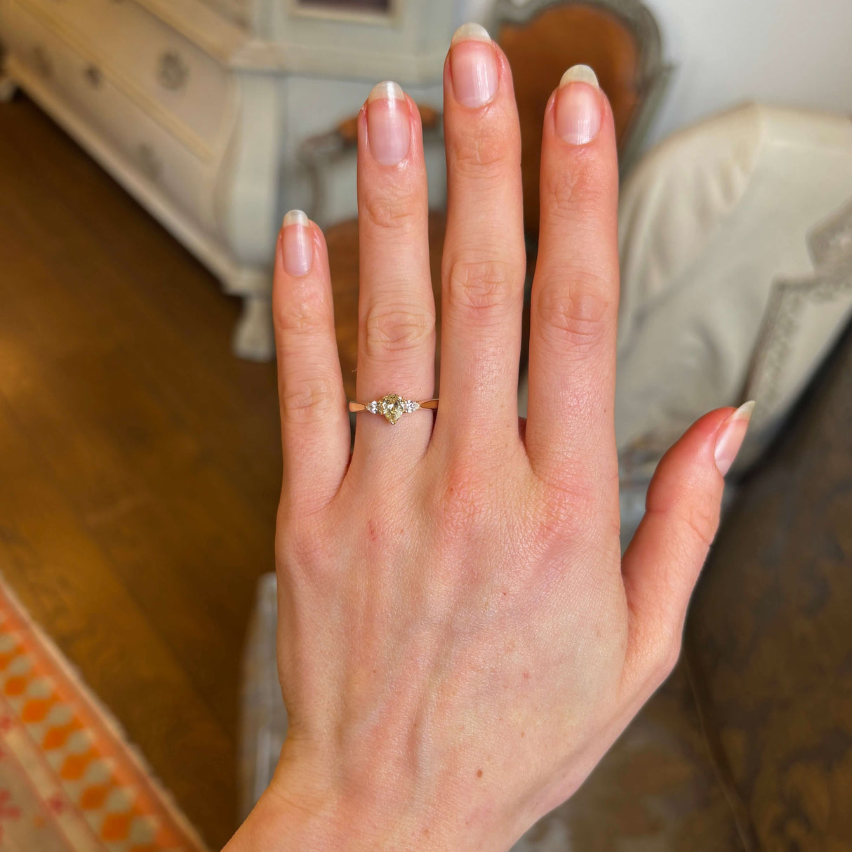 Pear-cut diamond three-stone engagement ring worn on hand at a distance to show scale. 