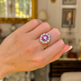 Pink sapphire and diamond cluster ring worn on closed hand.
