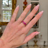 Five stone pink sapphire and yellow gold ring worn on hand with antiquated bokeh backgroundfront view
