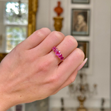 Five stone pink sapphire and yellow gold ring, worn on closed hand shot on antiquated bokeh background.