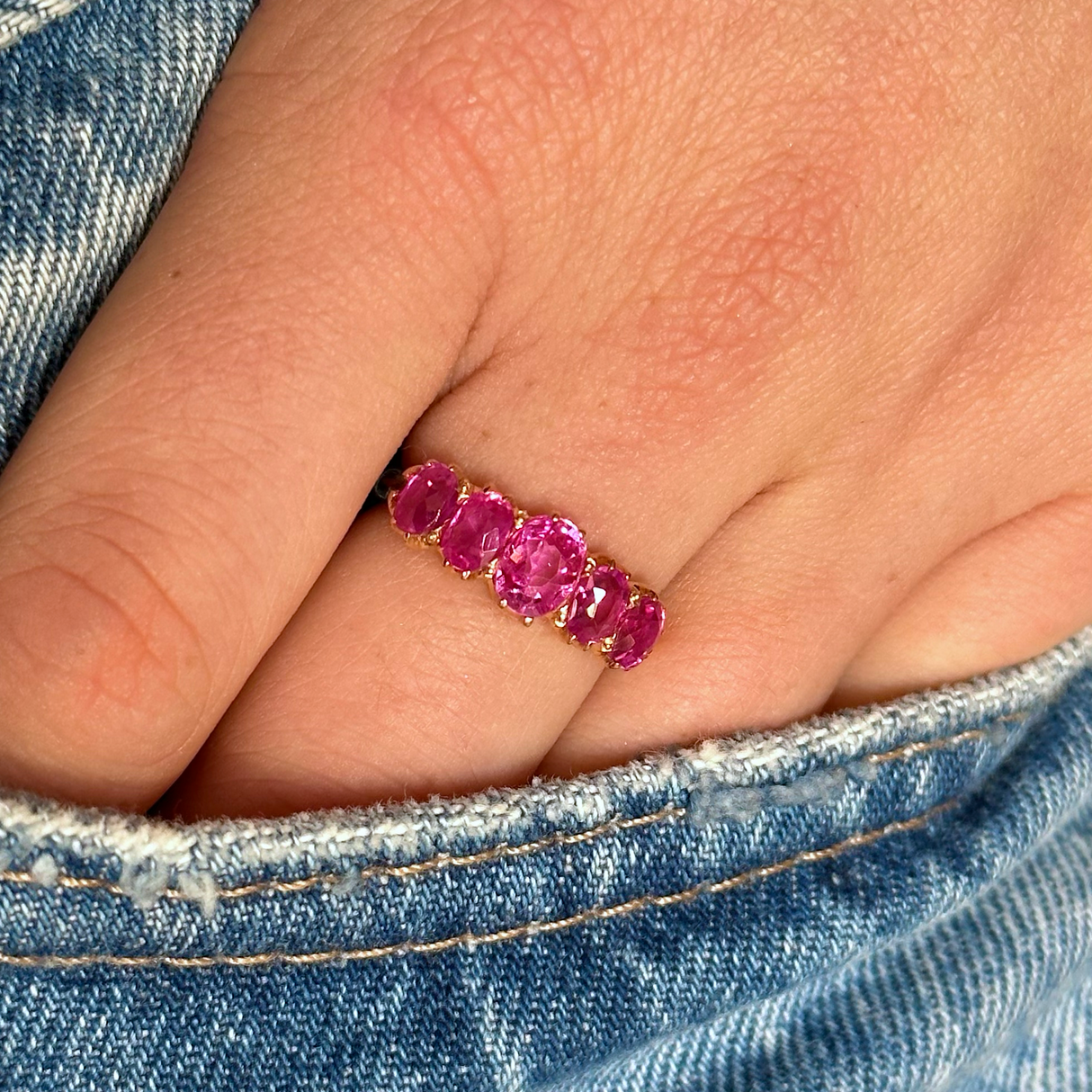 Five stone pink sapphire and yellow gold ring, hand in denim jeans