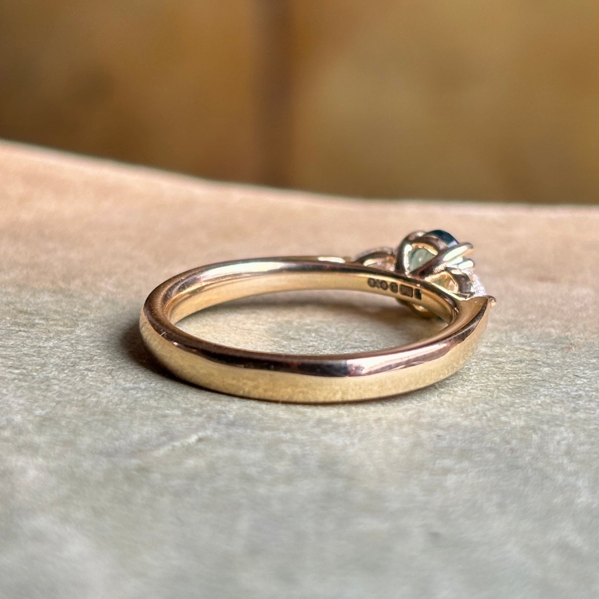 Reverse of the oval-cut teal sapphire and diamond three-stone engagement ring, clearly showing the hallmarks and maker’s marks on the band.
