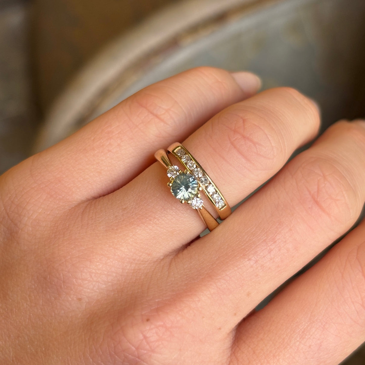 Round-cut teal sapphire and diamond three-stone engagement ring worn on the engagement ring finger, showing its elegance and fit.