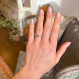 Round teal sapphire and pear-cut diamond three-stone engagement ring worn on the hand, illustrating its size and proportion.