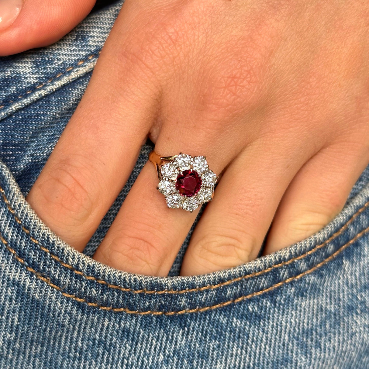antique ruby and diamond cluster ring worn on the middle finger on a hand placed into the pocket of denim jeans. 
