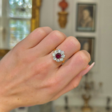 antique ruby and diamond cluster ring worn on the middle finger on a closed hand, shot with an antiquated bokeh background