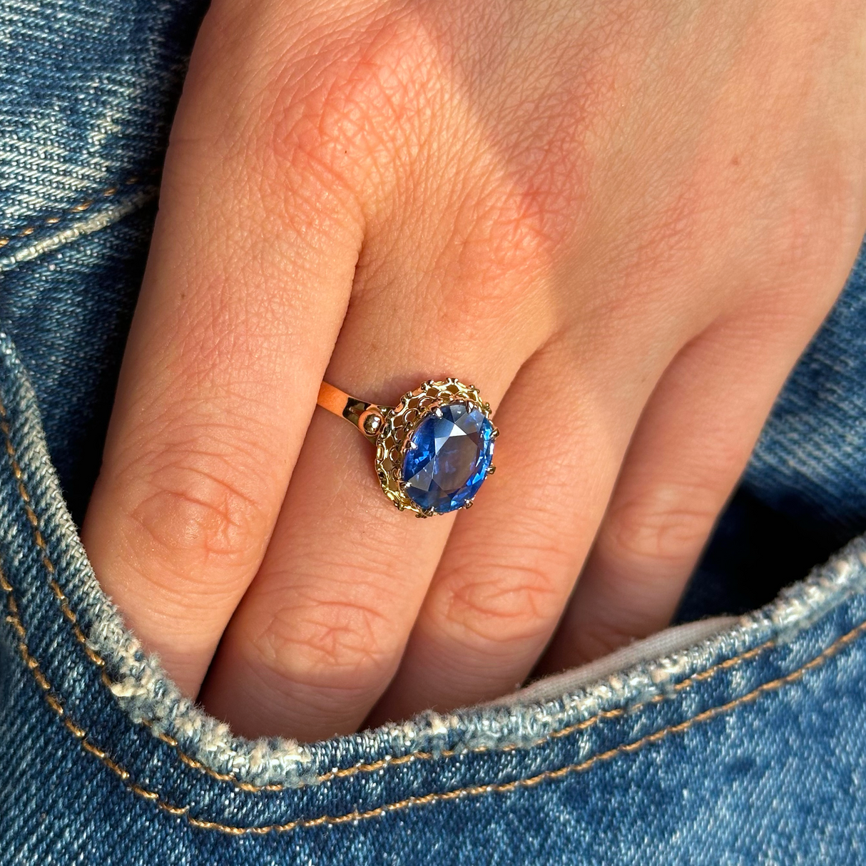 sapphire and yellow gold engagement ring worn on hand in pocket of jeans.