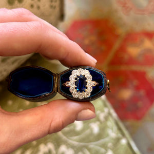 Hand holding a sapphire and diamond cluster ring in a blue ringbox