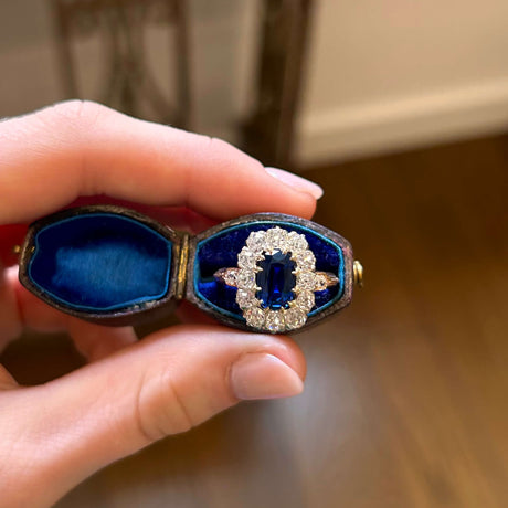 Sapphire and diamond cluster ring in a blue velvet box held in between fingers