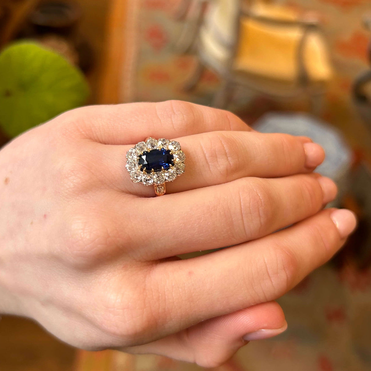 Hand wearing a sapphire and diamond cluster ring held up to see the proportions of ring