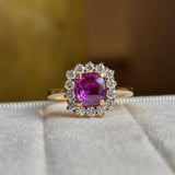 Square-cut pink sapphire and diamond cluster engagement ring placed on a white ring tray with a blurred background. 