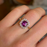 Square-cut pink sapphire and diamond cluster engagement ring worn on the ring finger of the left hand close up