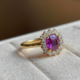 Square-cut pink sapphire and diamond cluster engagement ring placed on a white ring tray with a blurred background. 