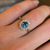 Teal sapphire and diamond cluster engagement ring captured up close on hand. 