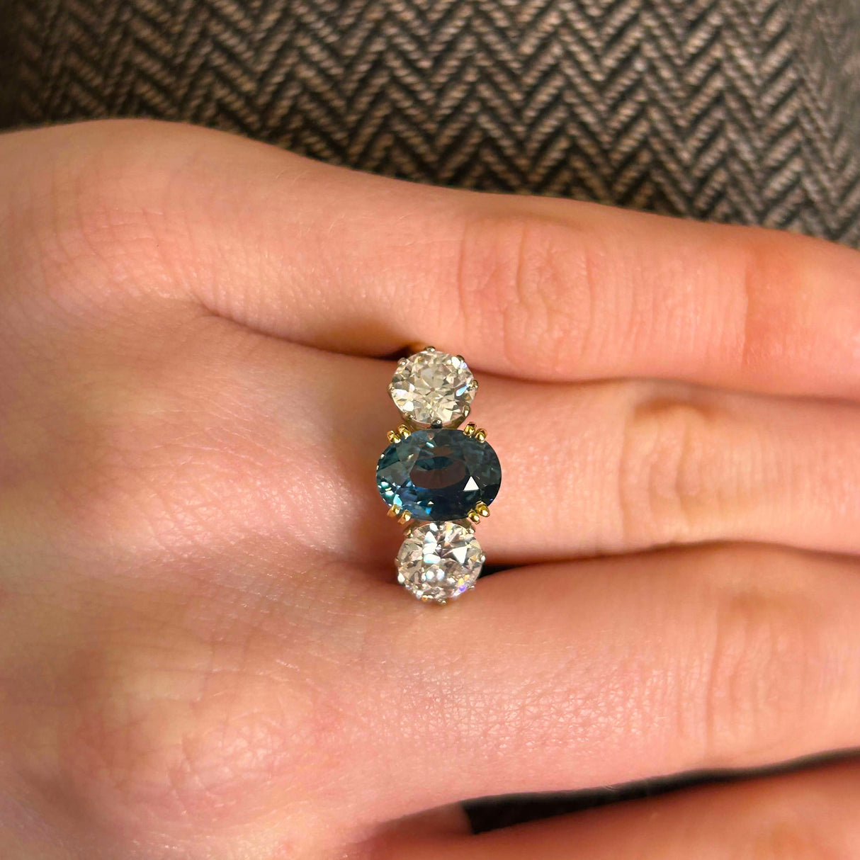 Close details of teal sapphire three-stone ring when worn on the hand