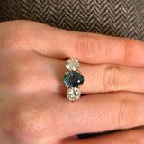 Close details of teal sapphire three-stone ring when worn on the hand