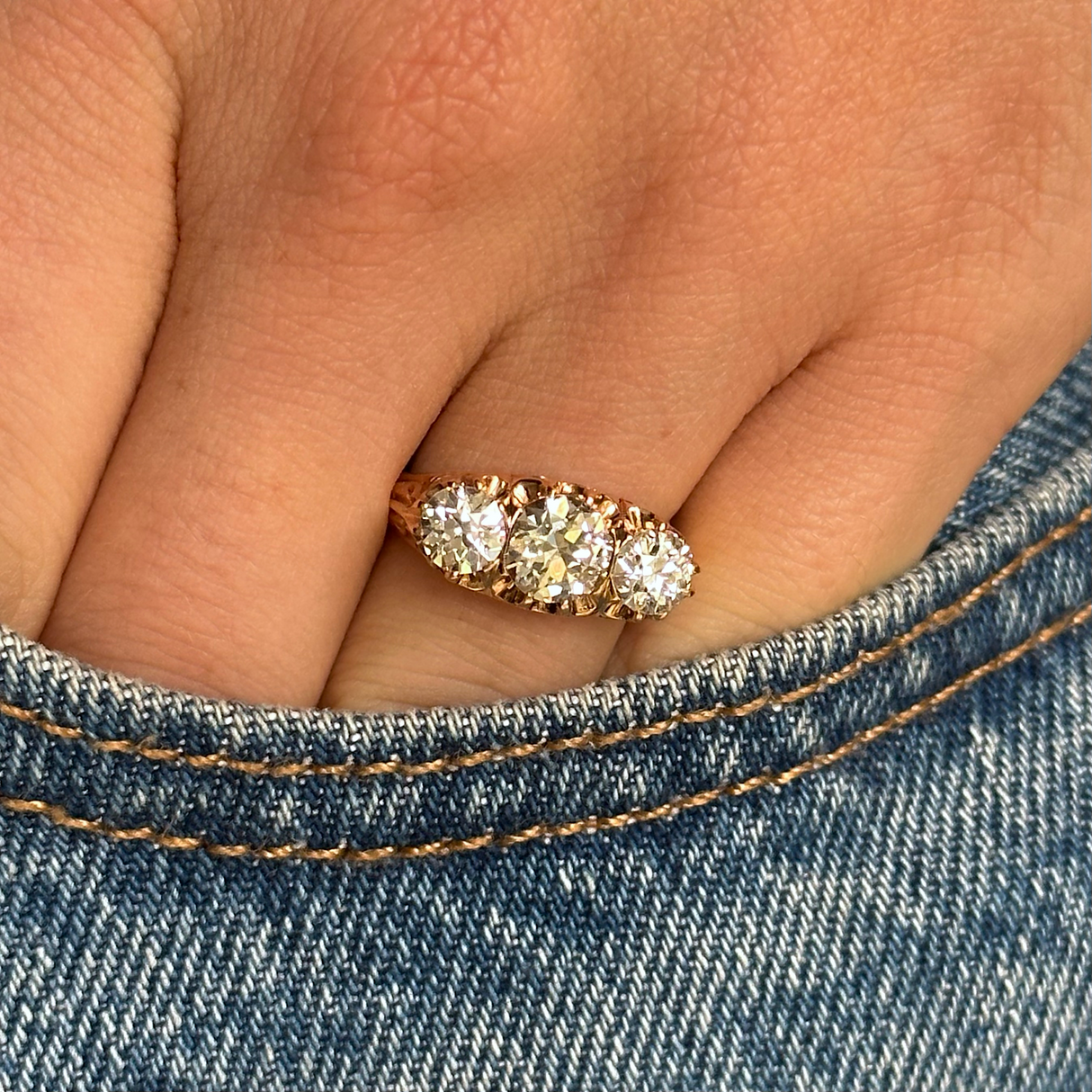 three stone antique italian diamond engagement ring, worn on hand and placed in pocket of denim jeans, front view. 