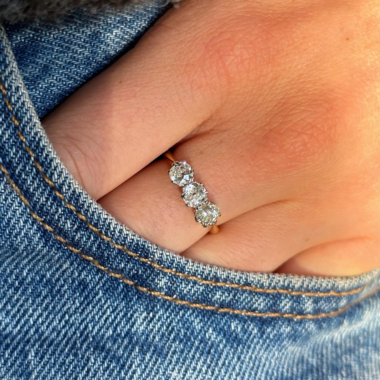 antique three stone diamond engagement ring, 18ct yellow gold band, worn on hand and placed in pocket of jeans, front view. 