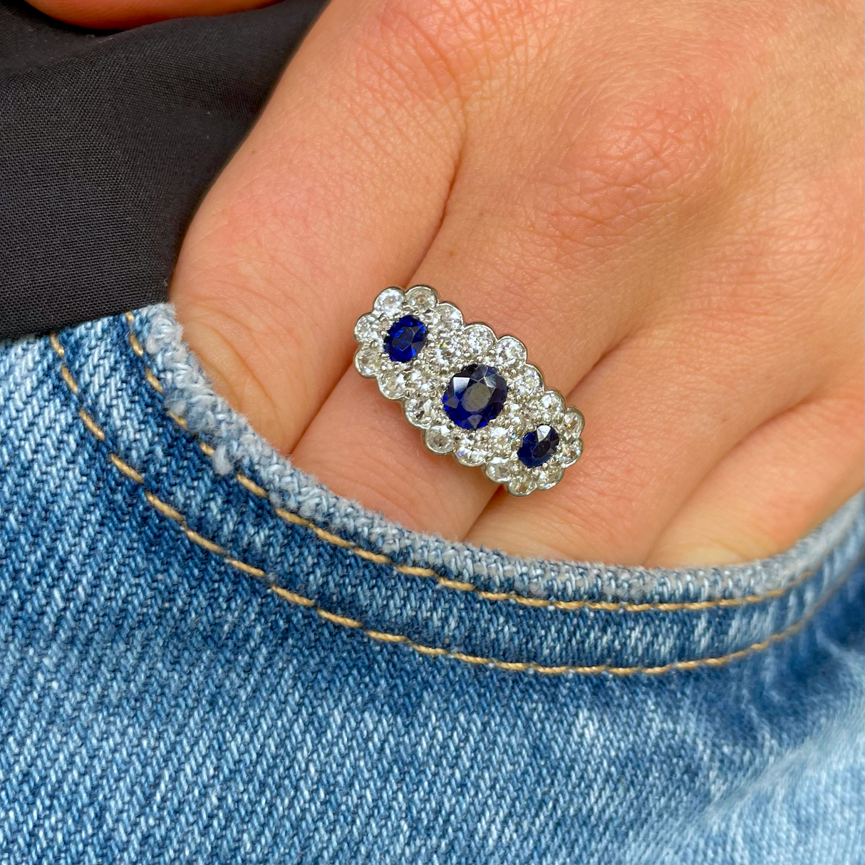 Antique sapphire and diamond triple cluster ring worn on hand.