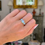 Opal and diamond three stone ring, worn on closed hand, front view. 