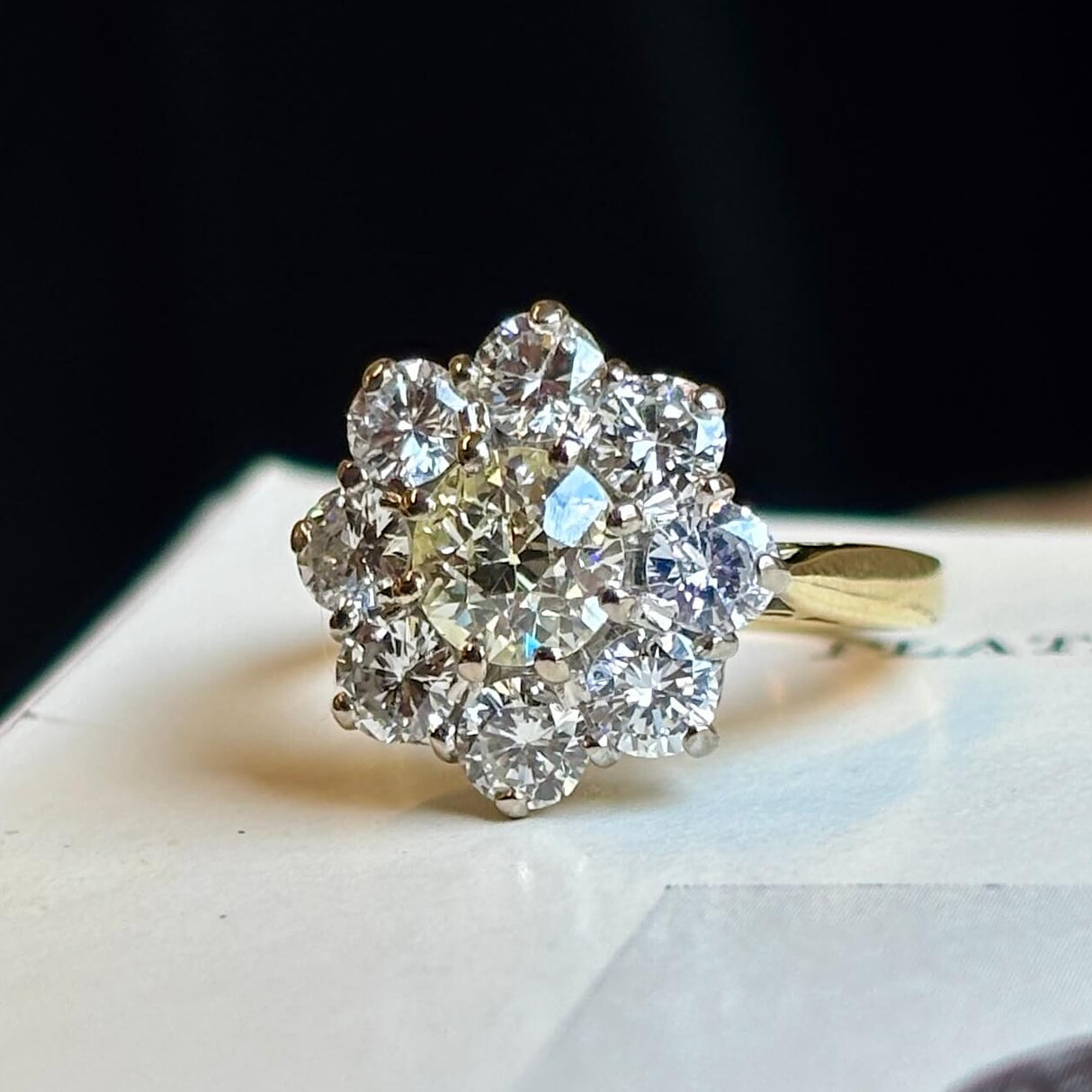 Vintage 1980s diamond cluster ring captured to show the diamonds colour, placed on a vintage book at a 45 degree angle to show proportions. 