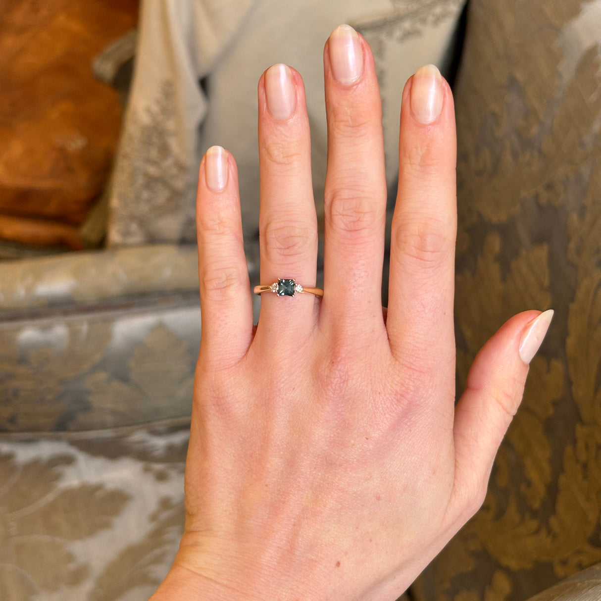 Vintage-inspired square-cut teal sapphire and diamond three-stone engagement ring worn on the hand.