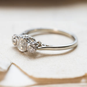 A three-stone old-cut diamond vintage engagement ring set in 18ct white gold displayed on a book. 