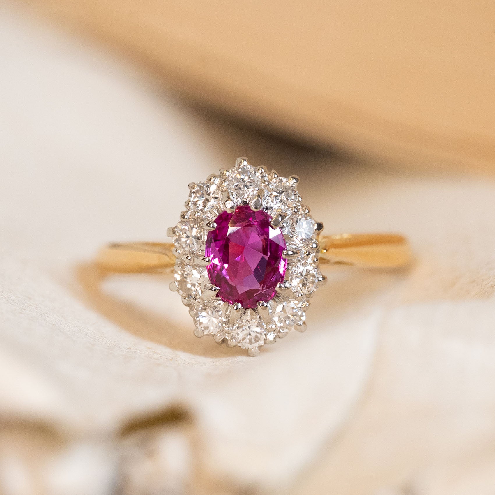 A vintage gold ring with a ruby and diamond cluster stones on a blurred background.