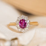A vintage gold ring with a ruby and diamond cluster stones on a blurred background.
