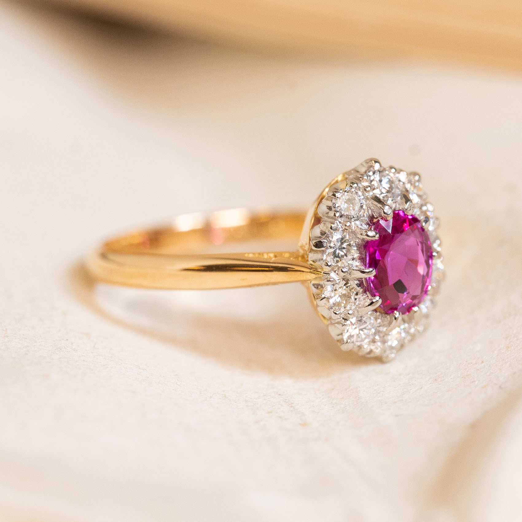 Vintage gold ring with a pink ruby gemstone and diamond halo on a light background.