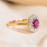 Vintage gold ring with a pink ruby gemstone and diamond halo on a light background.