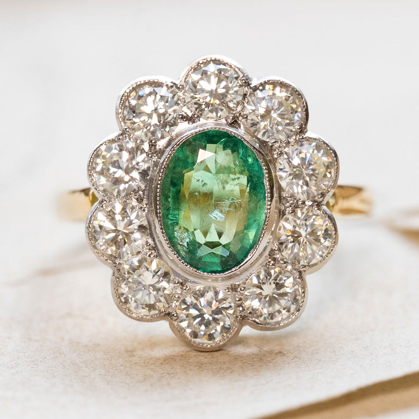 Vintage ring with a green emerald and diamond cluster on a soft paper background.