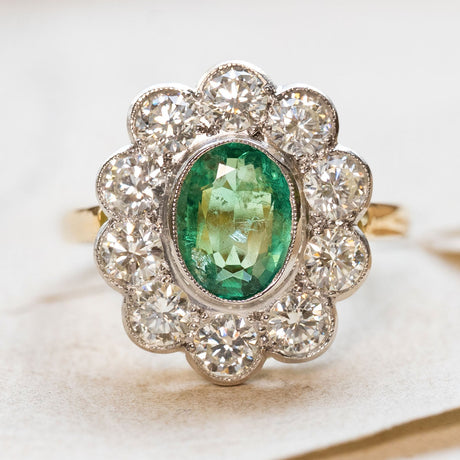 Vintage ring with a green emerald and diamond cluster on a soft paper background.