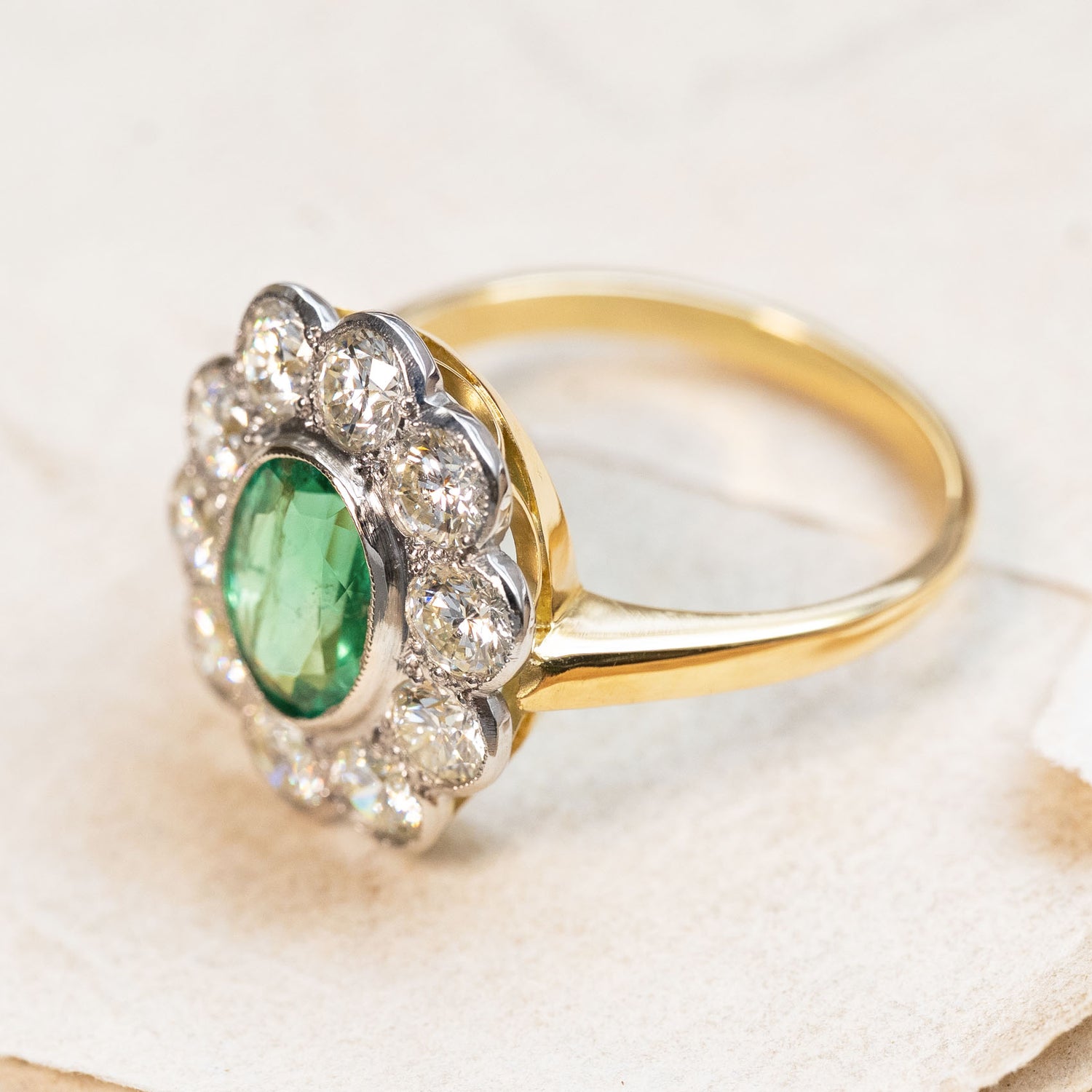 A vintage 1950s yellow and white gold ring with a green emerald gemstone and diamond halo. 